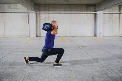 male athlete doing weighted lunges in a parking garage