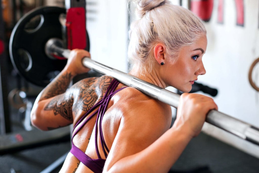 blonde female athlete with straight barbell racked on shoulders