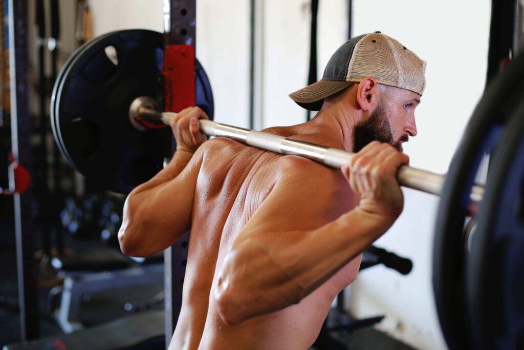 male athlete wearing a hat with straight barbell racked on shoulders