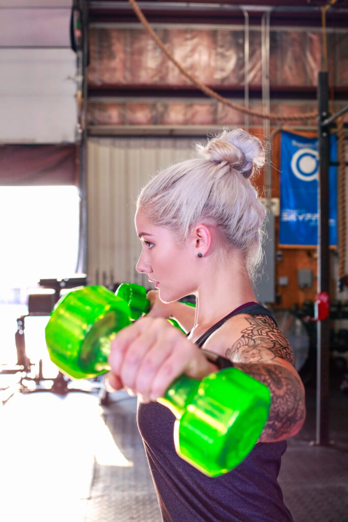 blonde female athlete with sleeve tattoos doing lateral raises with green jelly bells
