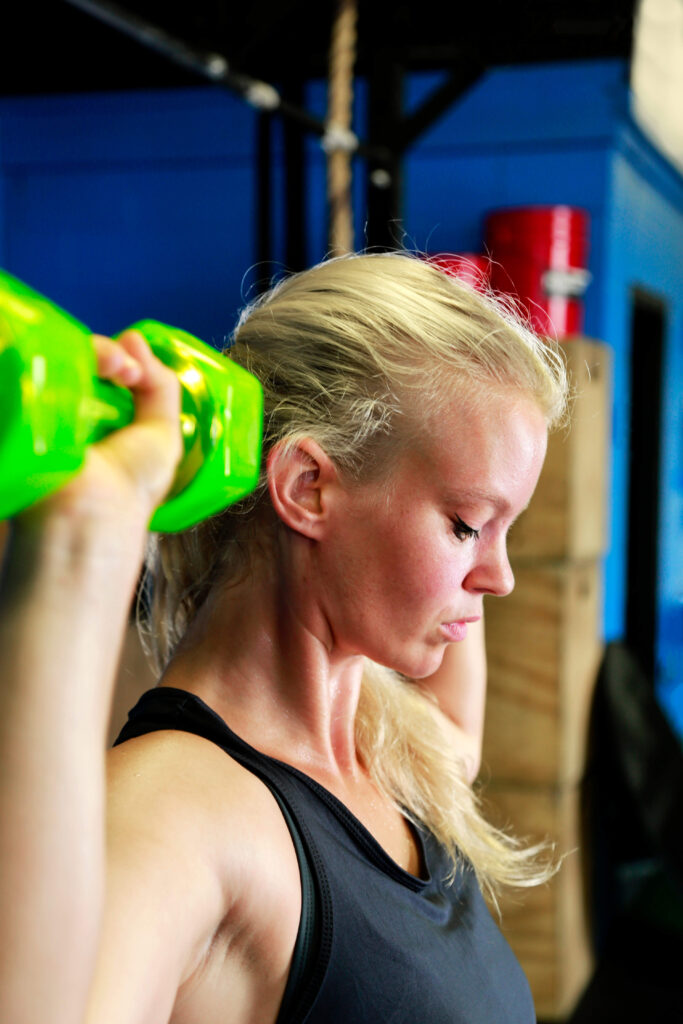 blonde female athlete doing shoulder presses with green jelly bells