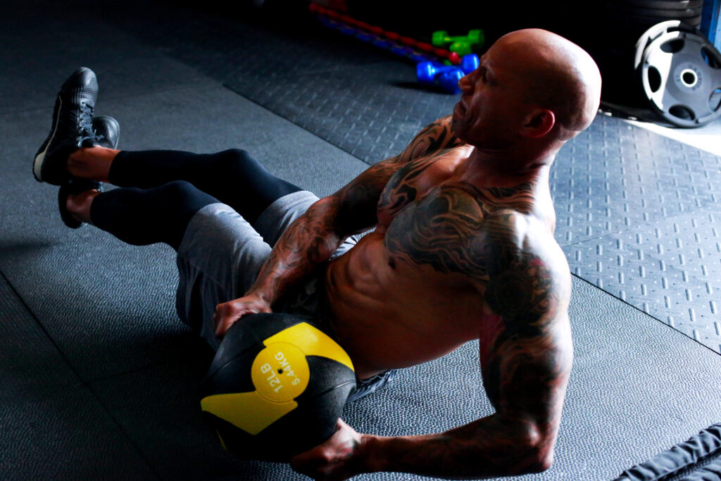 male athlete with sleeve tattoos doing an abdominal twist with a medicine ball